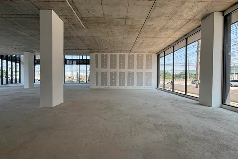 An unfinished open-plan floor with a bare concrete soffit and floor-to-ceiling glazing on two sides.