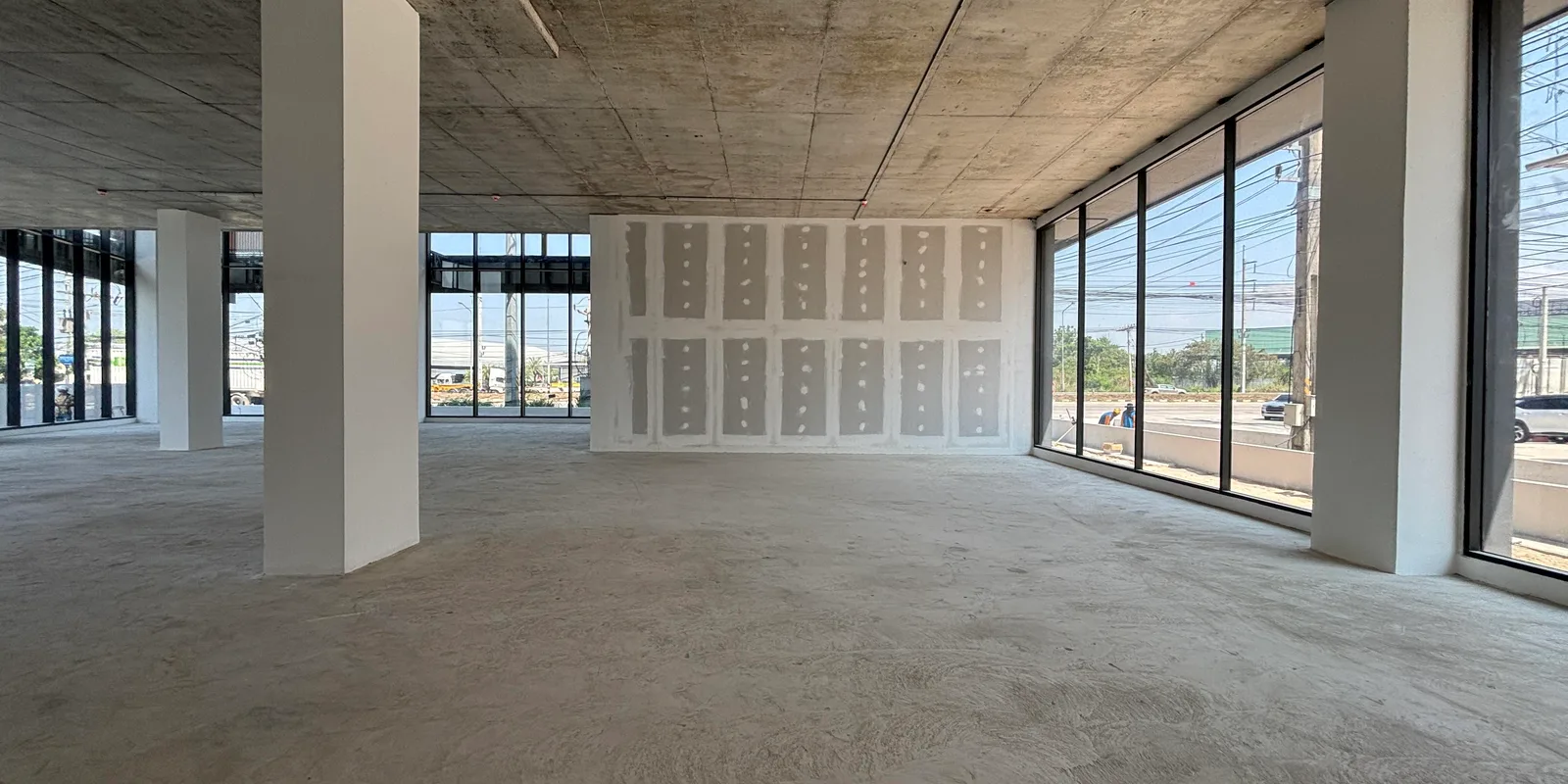 An unfinished open-plan floor with a bare concrete soffit and floor-to-ceiling glazing on two sides.