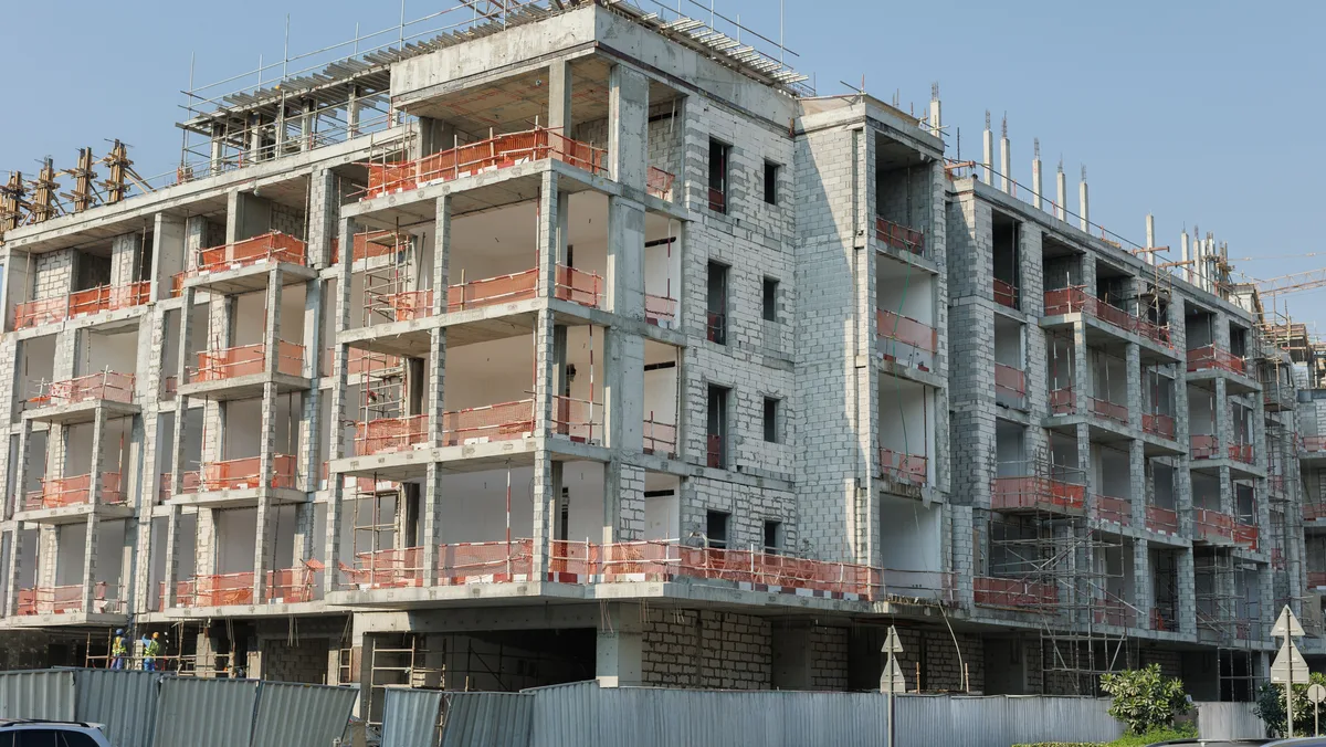 A multi-story concrete-frame building under construction behind scaffolding and site fencing.