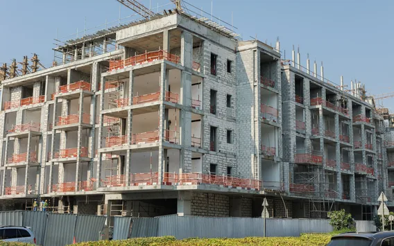 A multi-story concrete-frame building under construction behind scaffolding and site fencing.