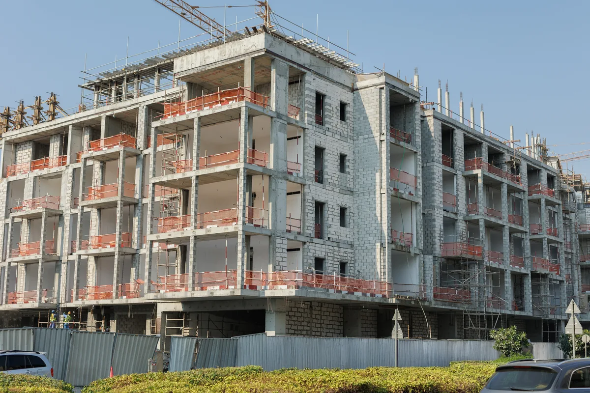 A multi-story concrete-frame building under construction behind scaffolding and site fencing.