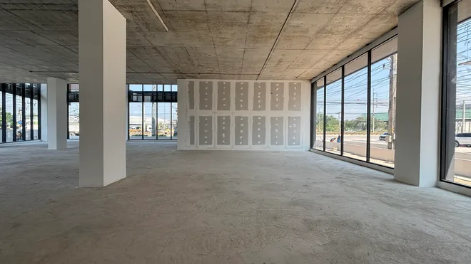 An unfinished open-plan floor with a bare concrete soffit and floor-to-ceiling glazing on two sides.