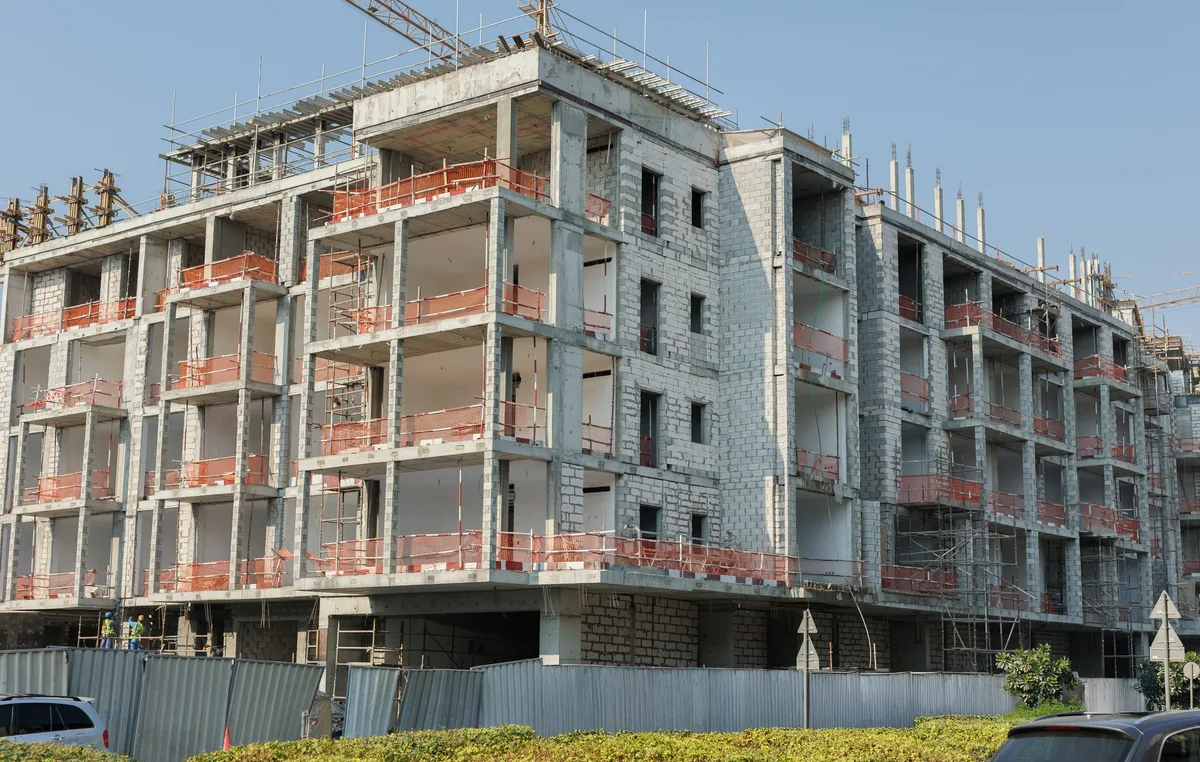 A multi-story concrete-frame building under construction behind scaffolding and site fencing.